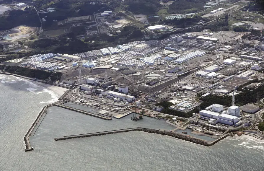 Luftaufnahme des Atomkraftwerks Fukushima an der Küste mit Reihen von Wassertanks und Hafenmolen im Meer – Ausgangspunkt der Debatte um eingeleitetes Kühlwasser